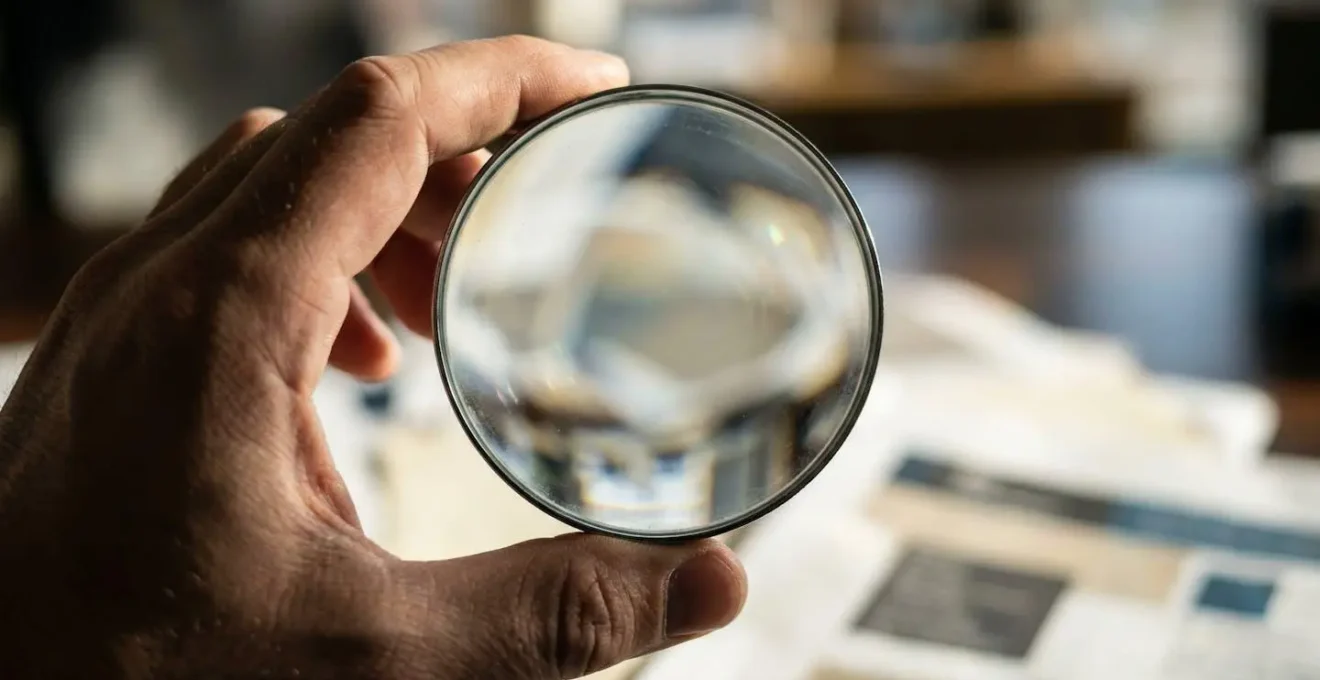 Gros plan sur une main tenant une loupe au-dessus de documents administratifs flous sur un bureau